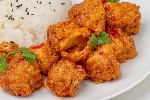 Close-up of spicy crispy chicken paired with jasmine rice garnished with sesame seeds and cilantro.