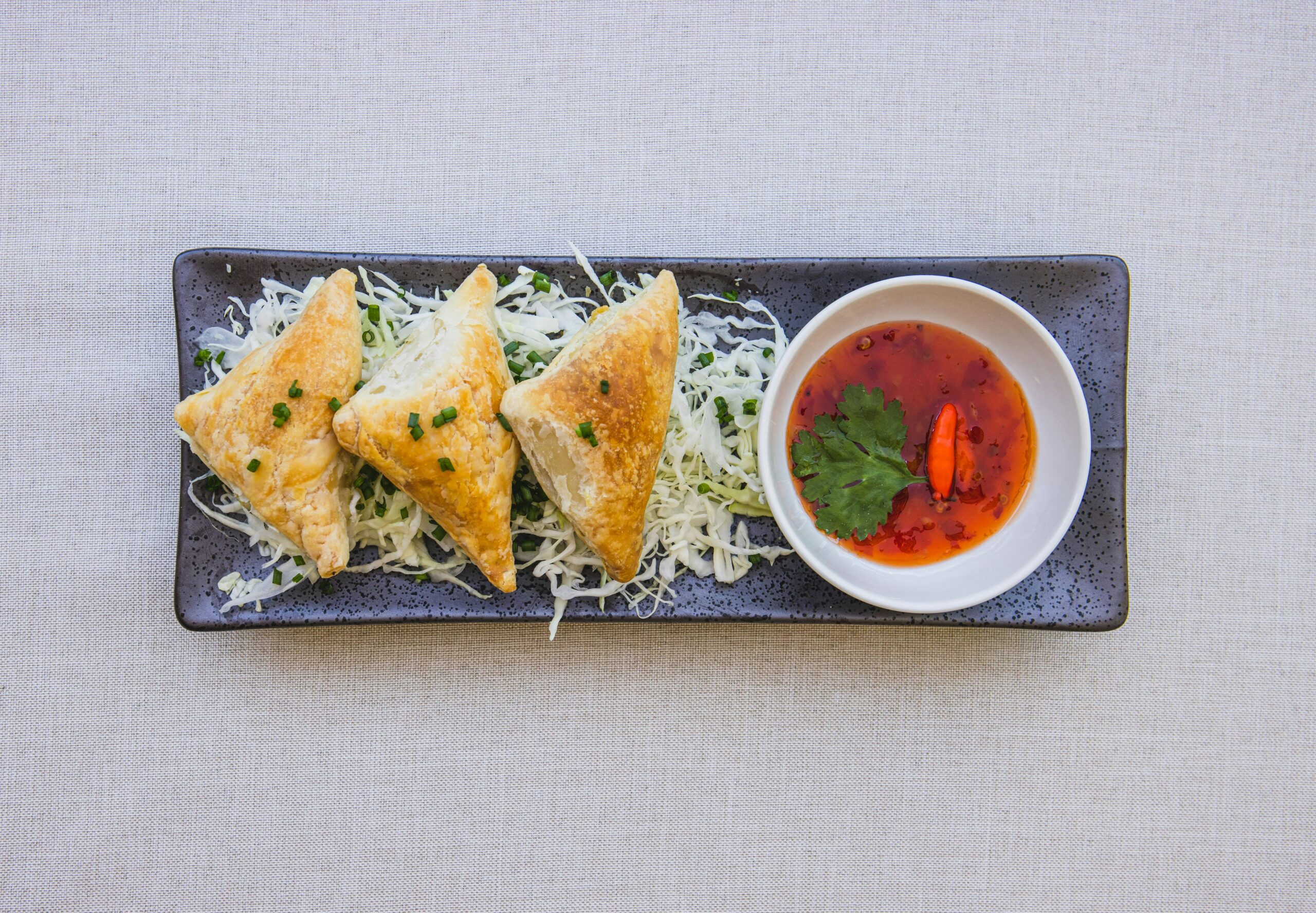 Top view of crispy samosas served with spicy red sauce, garnished with herbs.