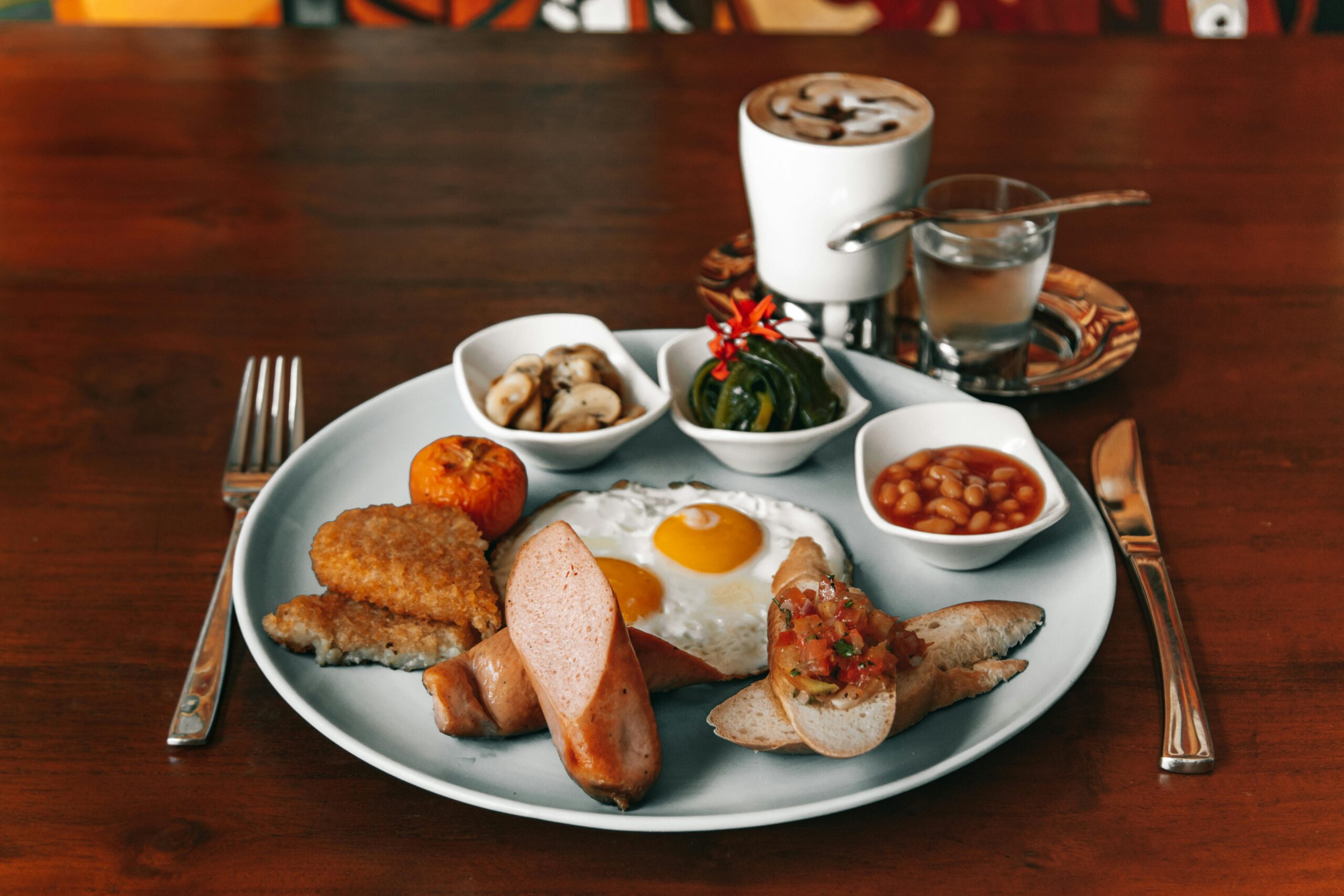 Delicious full breakfast plate with eggs, sausage, beans, and coffee on a wooden table.